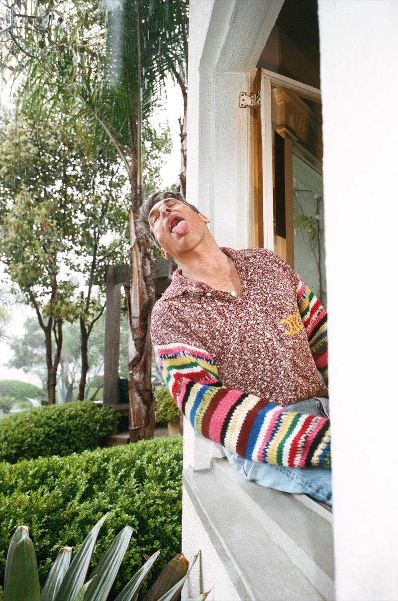 Jon leans out of a window wearing a striped polo sweater