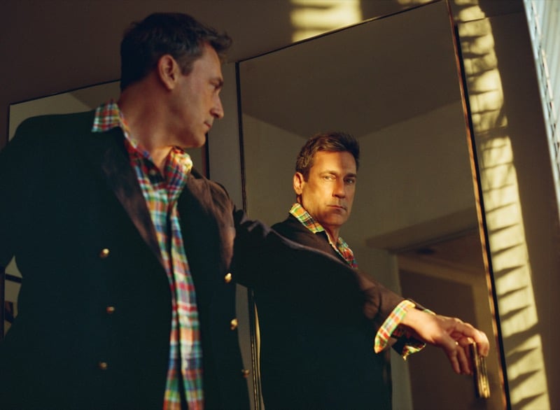 Jon looks at his reflection in a mirror wearing a double-breasted twill blazer and checked linen shirt