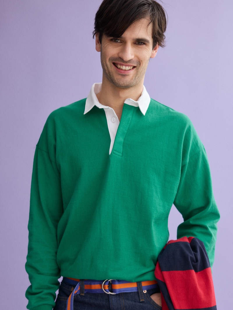 Dylan wears a J.Press x Alex Mill solid green rugby shirt with a white collar, paired with denim and an orange striped D-ring belt