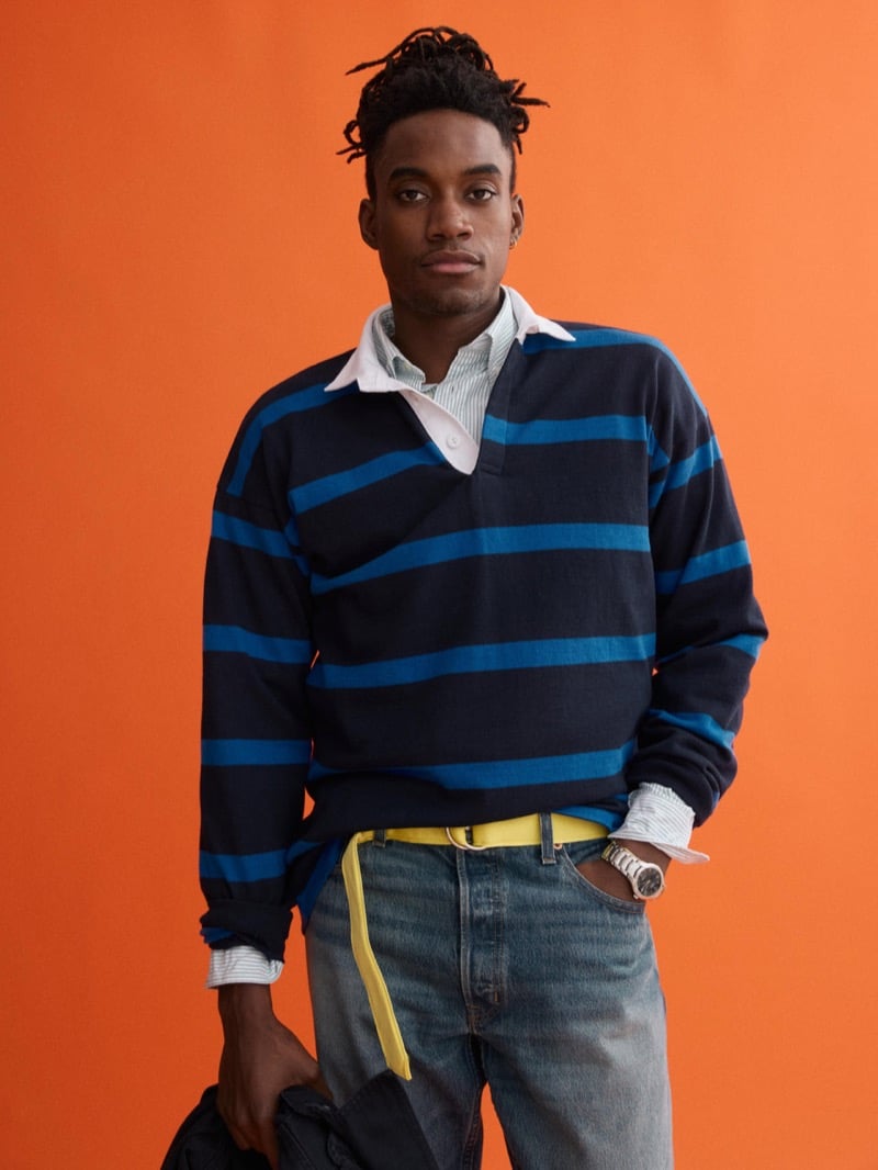 Herzen wears a J.Press x Alex Mill navy and blue striped rugby shirt over a striped button-down with washed denim and a yellow D-ring belt