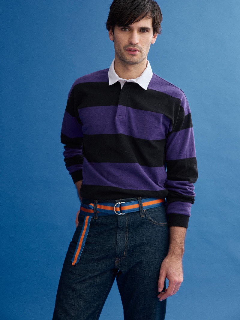 Dylan wears a J.Press x Alex Mill purple and black block-striped rugby shirt over a white collar shirt with dark jeans and a blue and orange D-ring belt