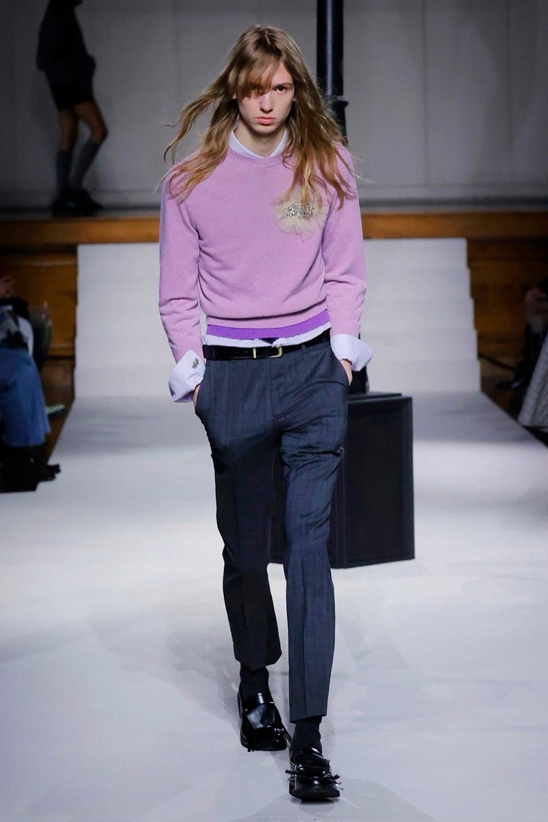 Kent & Curwen fall-winter 2026 lilac crewneck sweater with gold brooch over a lavender shirt with exaggerated cuffs and charcoal trousers