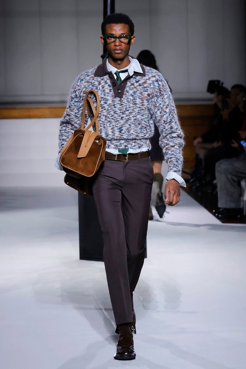 Kent & Curwen fall-winter 2026 marled knit polo sweater over a white shirt with charcoal trousers, a green tie, and a tan suede bag