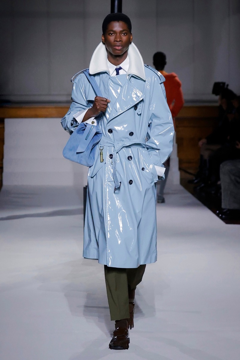 Kent & Curwen fall-winter 2026 powder blue patent leather belted trench coat over a white wide-collar shirt with olive trousers