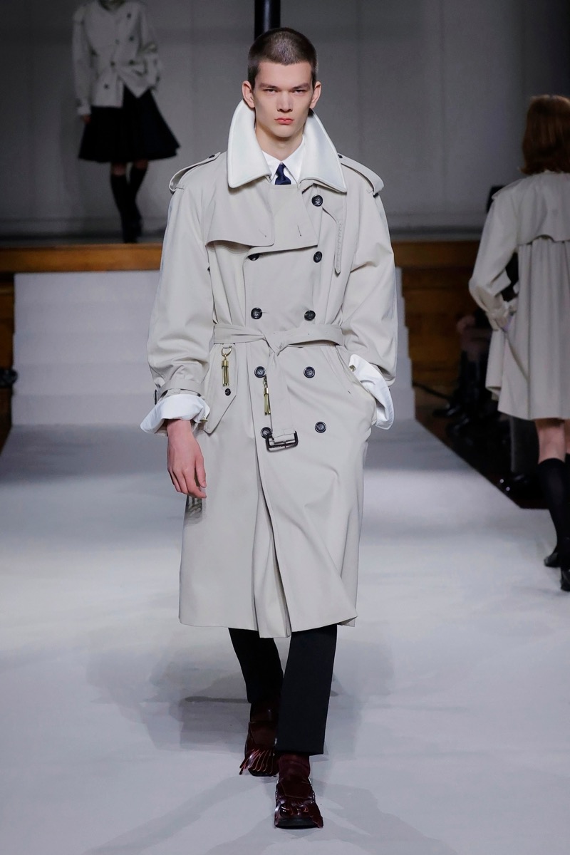 Kent & Curwen fall-winter 2026 stone double-breasted trench coat with brass hardware over a white shirt with a navy tie and black trousers