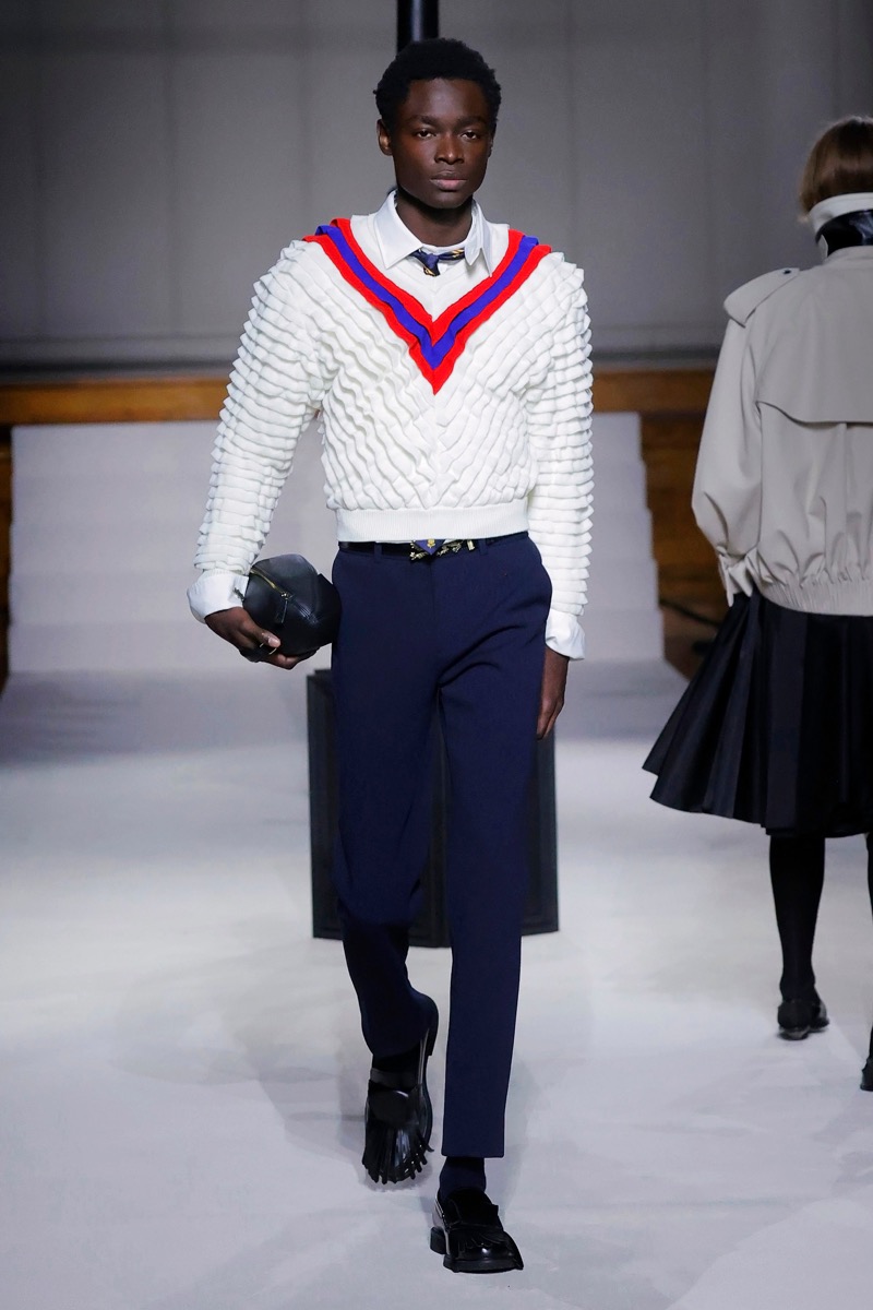 Kent & Curwen fall-winter 2026 white textured cricket sweater with red and blue V-stripe over a white shirt and navy cropped trousers
