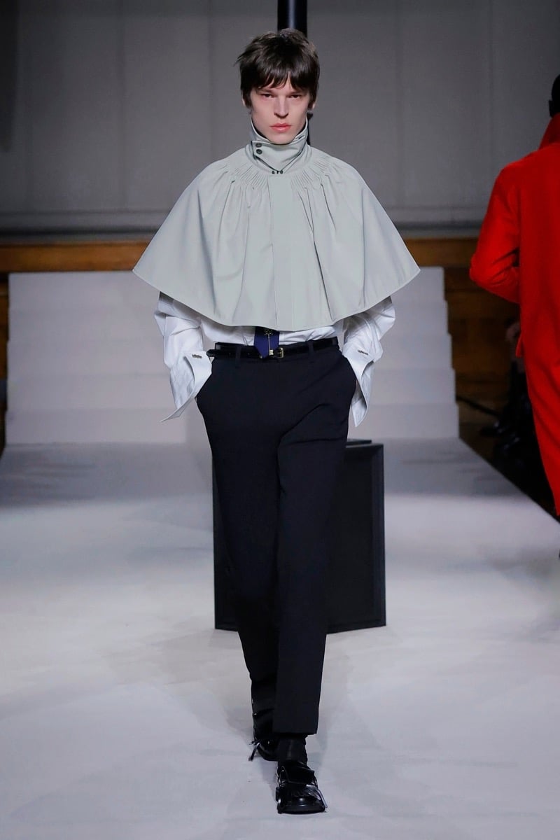 Kent & Curwen fall-winter 2026 pale gray gathered cape with pleated high collar over a white shirt and black trousers