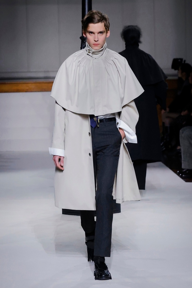 Kent & Curwen fall-winter 2026 stone caped overcoat with gathered collar over a white shirt and navy pinstripe trousers
