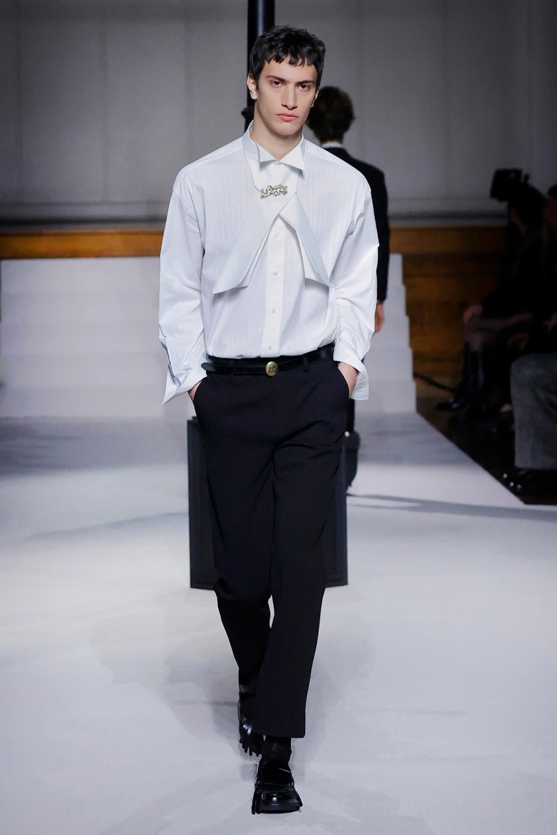 Kent & Curwen fall-winter 2026 white dress shirt with layered bib front and gold brooch over black trousers