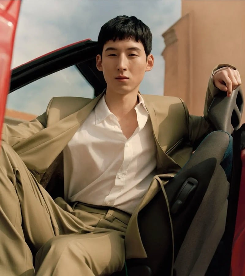 Woosang reclines in the open doorway of a red convertible car in a soft olive suit worn over an unbuttoned white shirt for Kenzo's pre-fall 2026 campaign