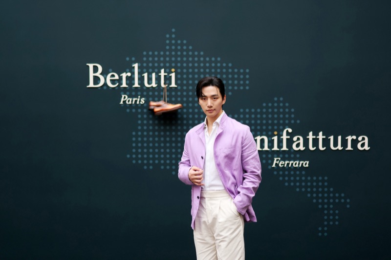 Lee Jun Ho stands in a lilac Forestière jacket and cream trousers in front of a Berluti world map backdrop
