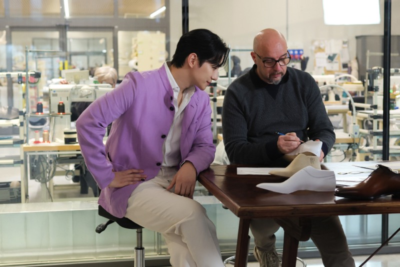 Jun-ho sits beside an artisan examining a shoe pattern inside the Berluti Manifattura in Ferrara