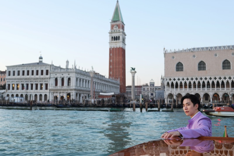 Jun-ho leans on the railing of a boat on the Venice Grand Canal with St. Mark's Campanile and the Doge's Palace behind him