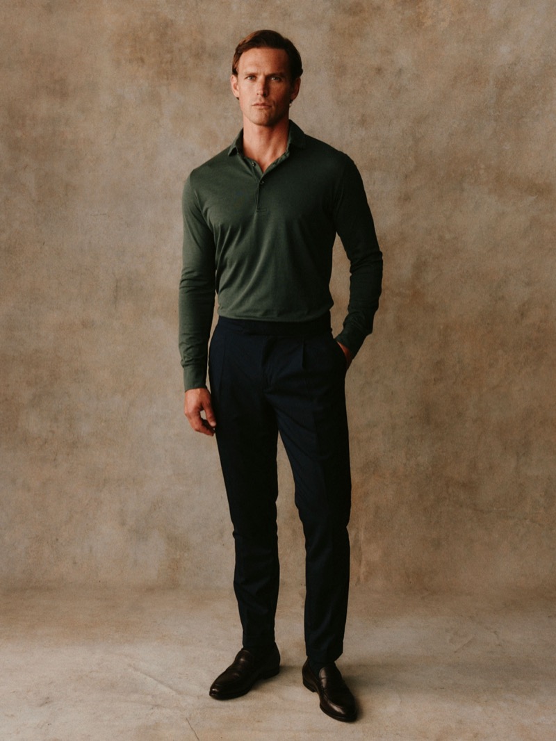 Guy wears a dark green long-sleeve polo with navy trousers and dark loafers