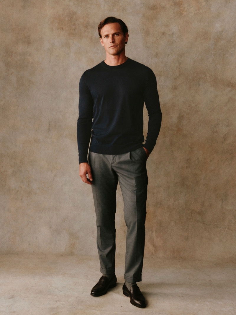 Guy wears a navy fine-knit crewneck sweater with gray trousers