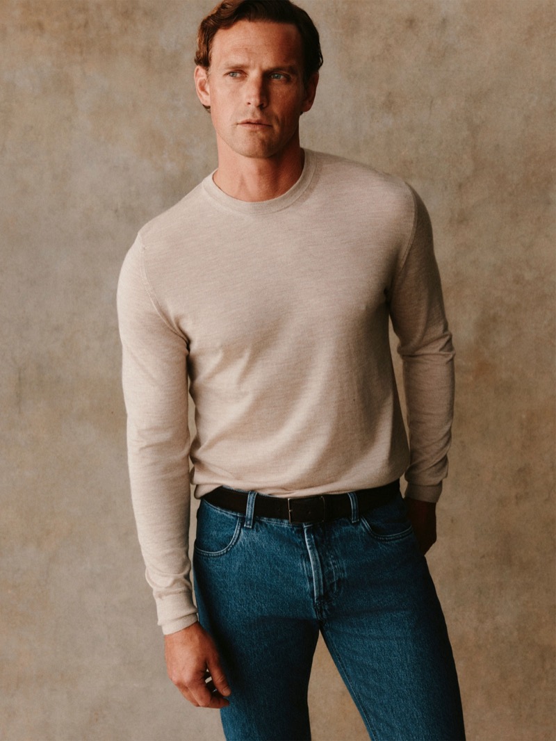 Guy wears a stone crewneck sweater with blue jeans and a leather belt