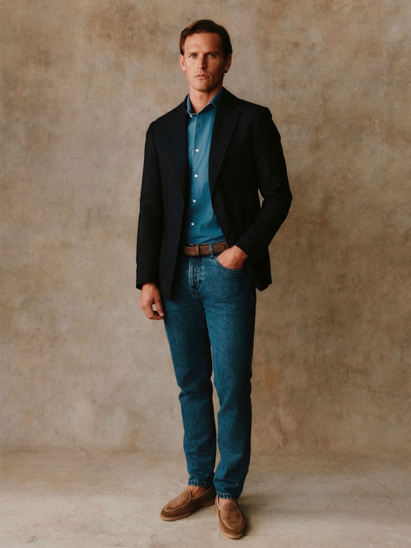 Guy wears a navy blazer over a teal denim shirt with blue jeans and suede loafers