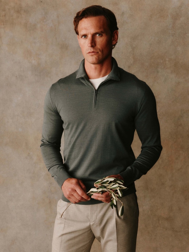Guy wears a sage green quarter-zip sweater with stone trousers