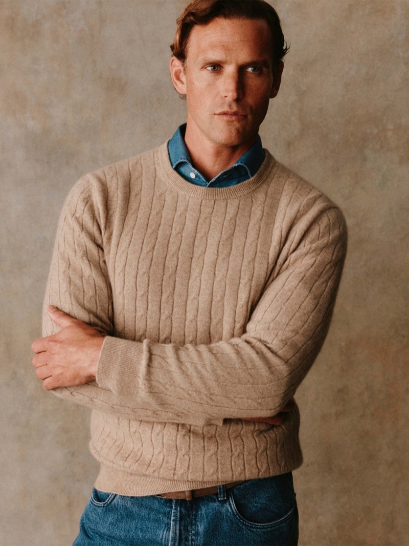 Guy wears an oatmeal cable-knit crewneck sweater over a denim shirt with jeans