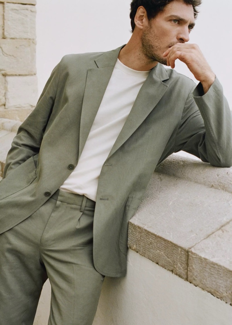 Pierre-Benoit wears a sage green suit with a white crew neck at a Mediterranean sea wall
