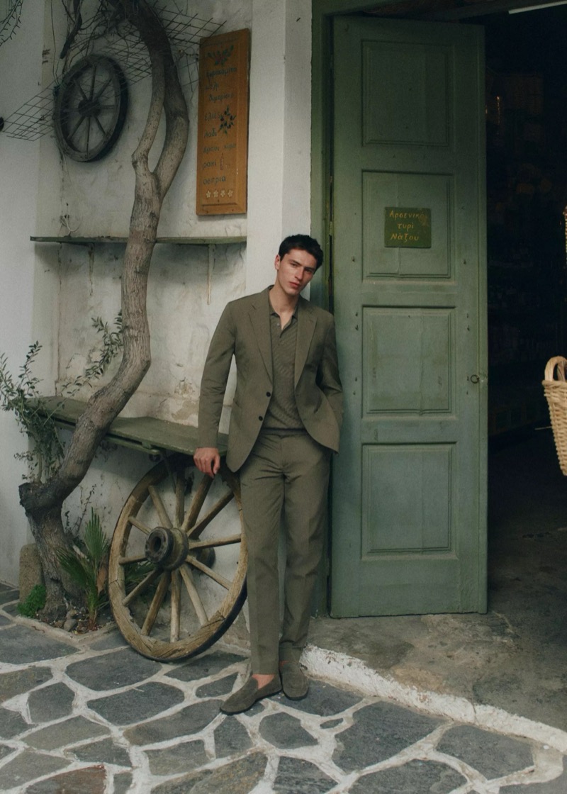 Clément leans in the doorway of a Greek storefront in an olive linen suit over a tonal knit polo with suede loafers for Mango Selection's spring-summer 2026 collection