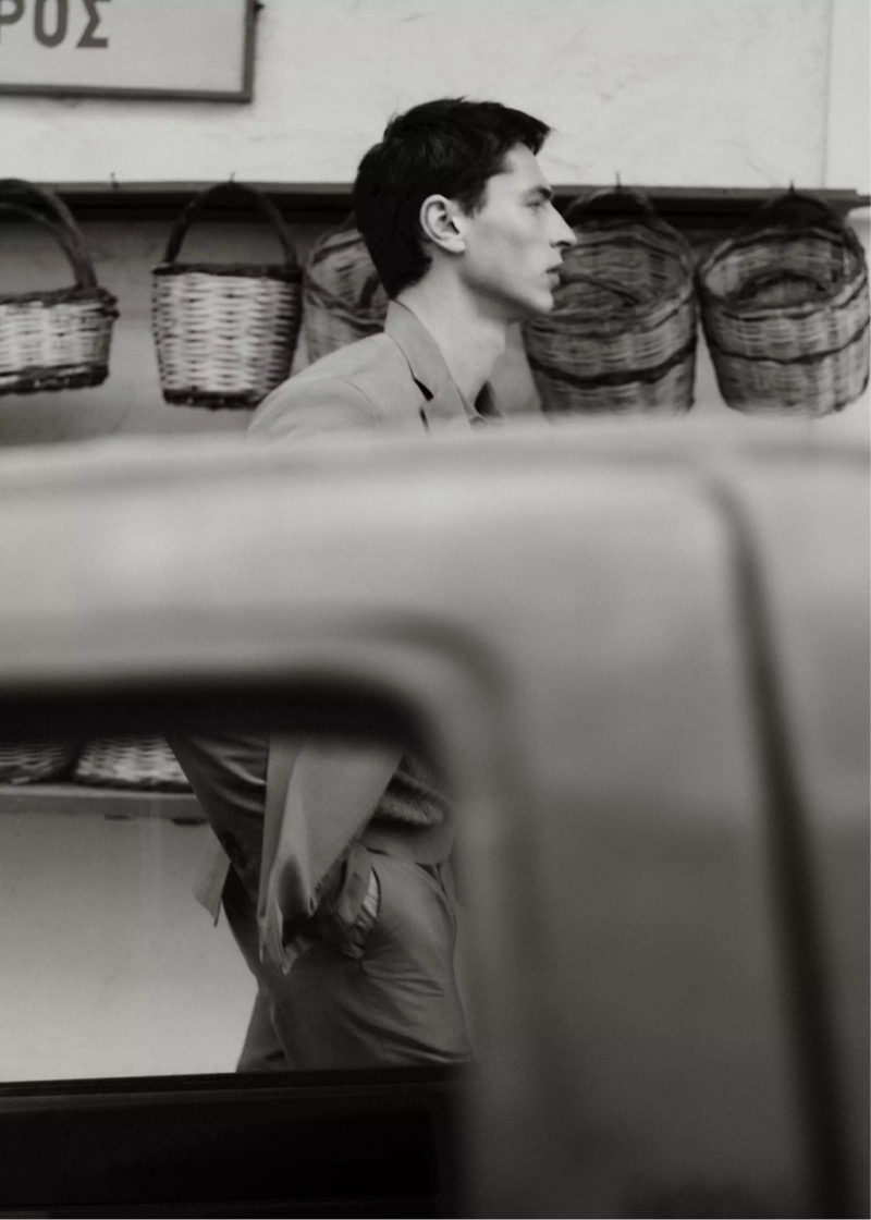 Black and white profile of Clément in a light suit walking past woven baskets in a Greek shop for Mango Selection's spring-summer 2026 collection