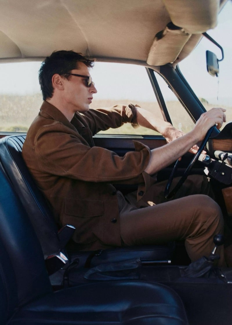 Clément drives a vintage car through an open landscape in a brown suede field jacket and brown trousers with sunglasses for Mango Selection's spring-summer 2026 collection