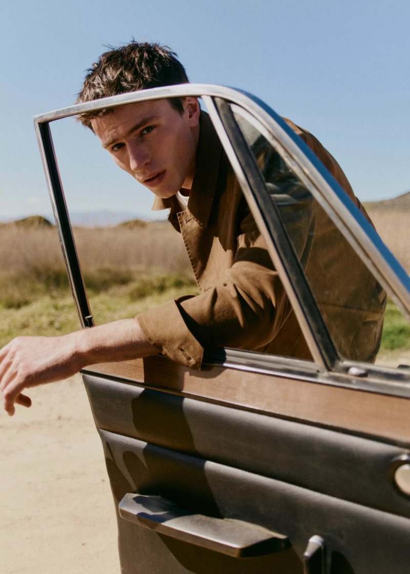 Clément leans out of the open door of a vintage car in a tan field jacket against a sunlit field for Mango Selection's spring-summer 2026 collection