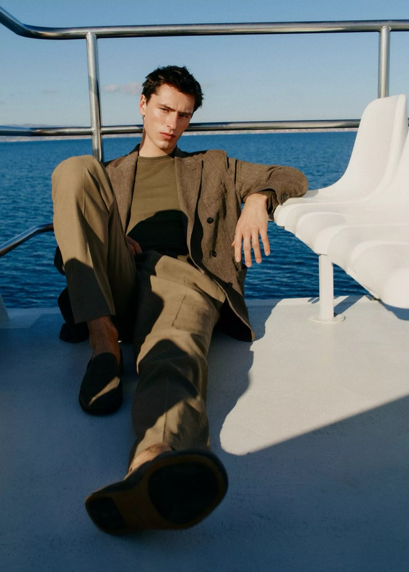 Clément reclines on the deck of a boat at sea in a taupe linen suit over an olive crew neck with suede loafers for Mango Selection's spring-summer 2026 collection