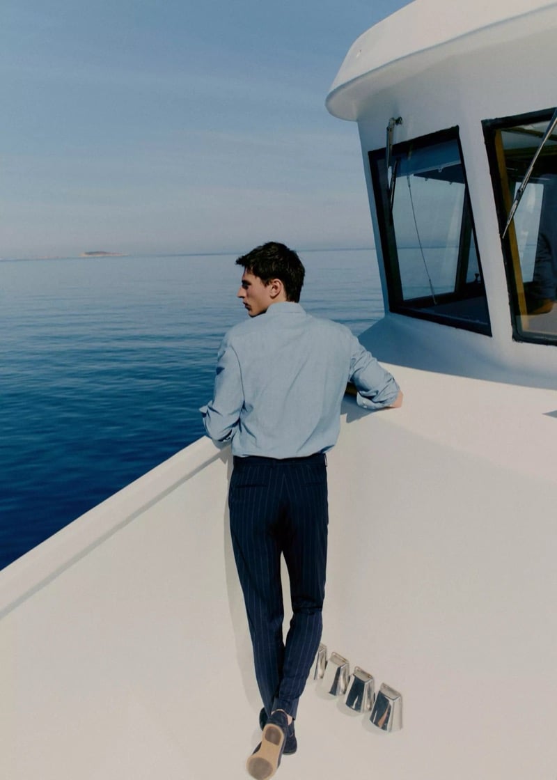 Clément walks toward the bow of a yacht in a denim-blue shirt and navy pinstripe trousers with blue suede loafers for Mango Selection's spring-summer 2026 collection