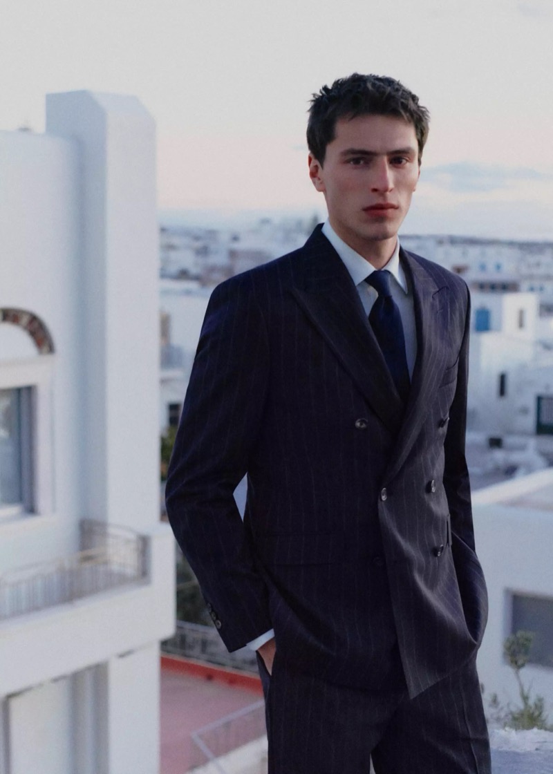 Clément stands on a rooftop above a Greek town in a navy pinstripe double-breasted suit with a white shirt and navy tie for Mango Selection's spring-summer 2026 collection