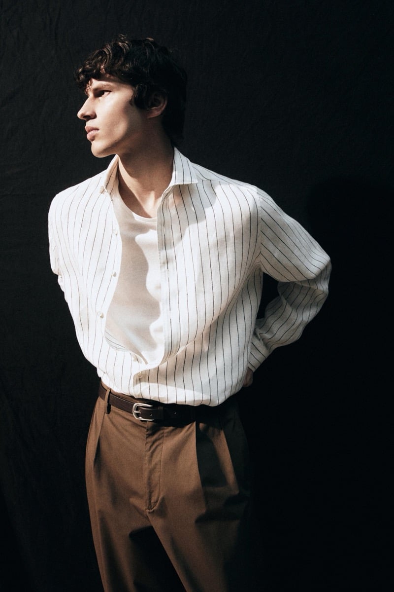 Kaplan wears a white pinstripe shirt open over a white tee with brown pleated trousers