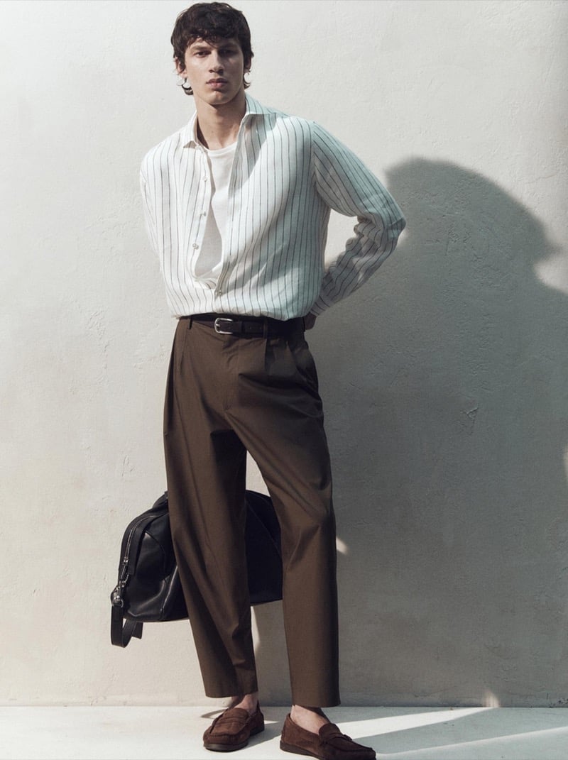 Kaplan wears a white pinstripe shirt with brown trousers and suede loafers