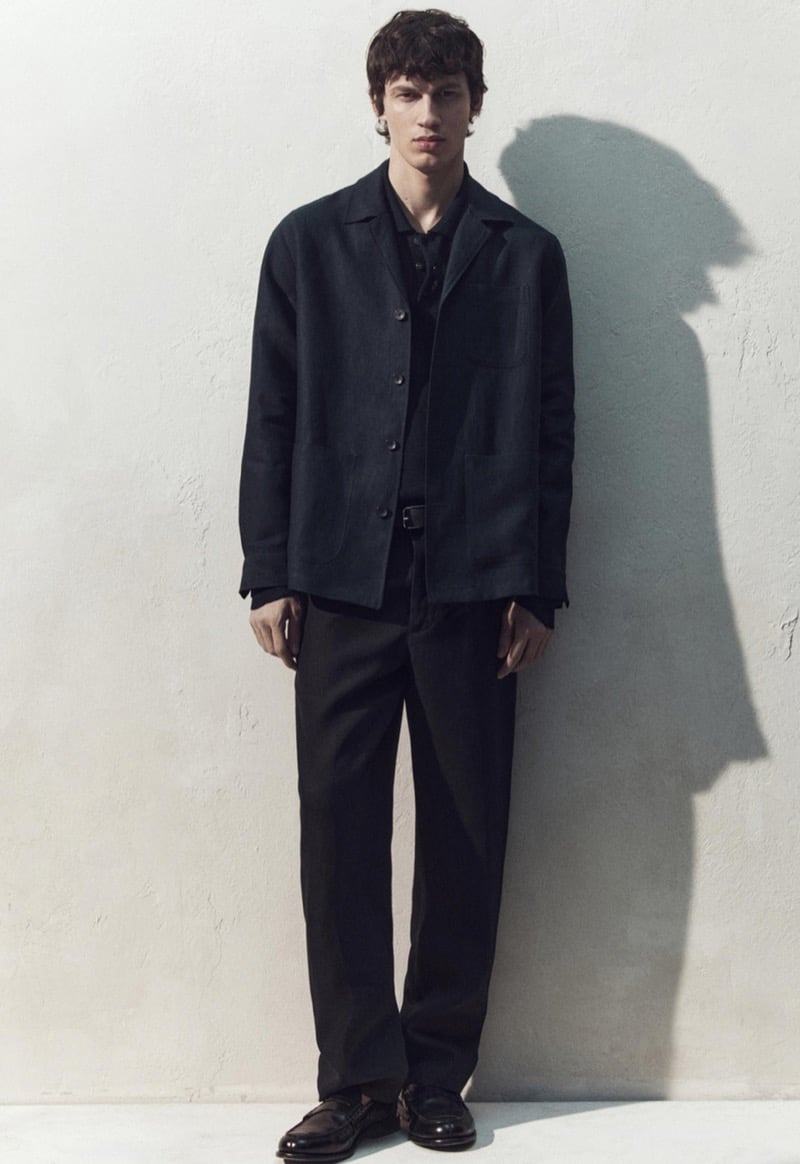 Kaplan wears a dark navy chore jacket with patch pockets and tonal trousers