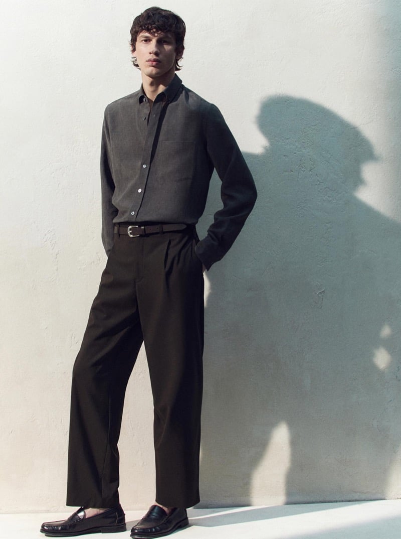 Kaplan wears a charcoal button-down shirt with brown pleated trousers