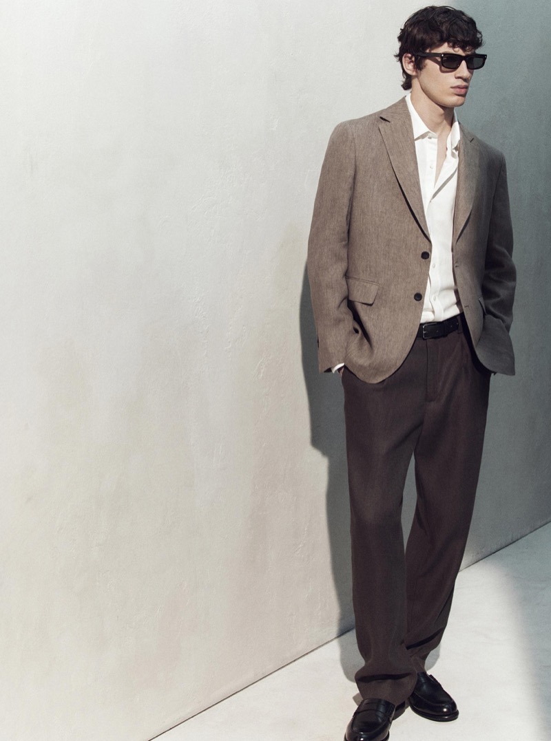 Kaplan wears a tan linen blazer over a white shirt with brown trousers and sunglasses