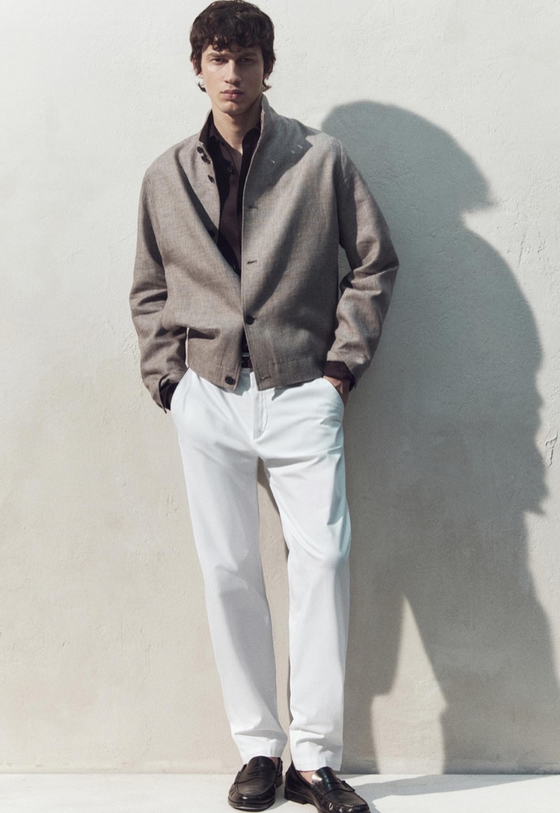 Kaplan wears a taupe jacket over a dark shirt with white trousers
