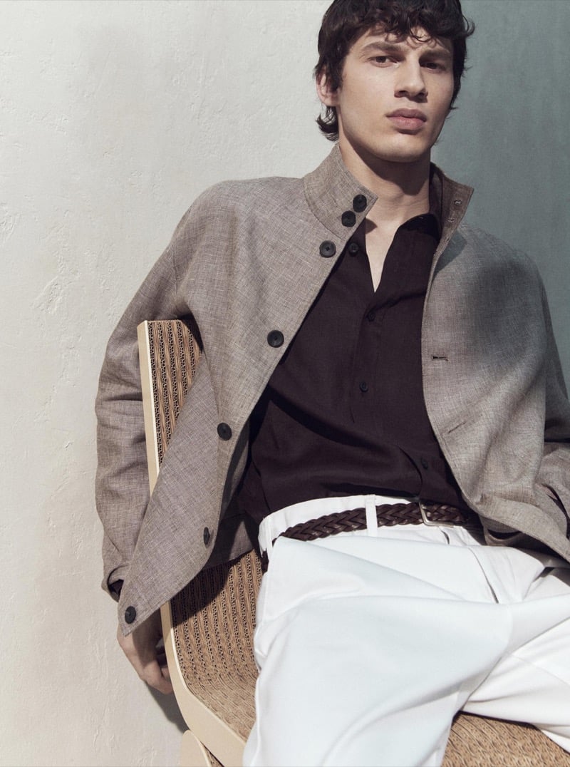 Kaplan wears a taupe jacket with a dark polo and white trousers while seated