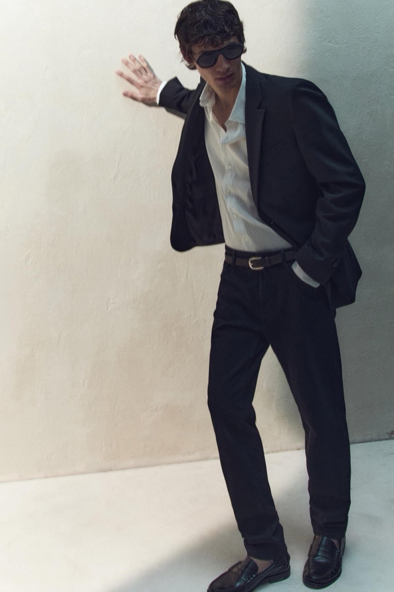 Kaplan wears a black blazer over a white shirt with dark trousers and sunglasses