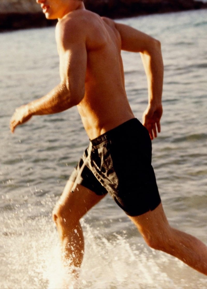 Valentin runs through shallow water in printed Massimo Dutti swim shorts at golden hour