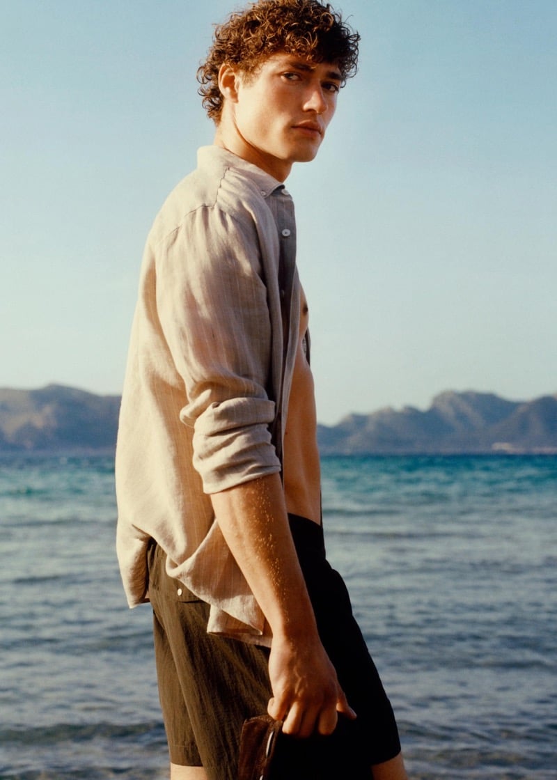 Valentin wears a linen shirt over dark Massimo Dutti swim shorts by the Mediterranean Sea