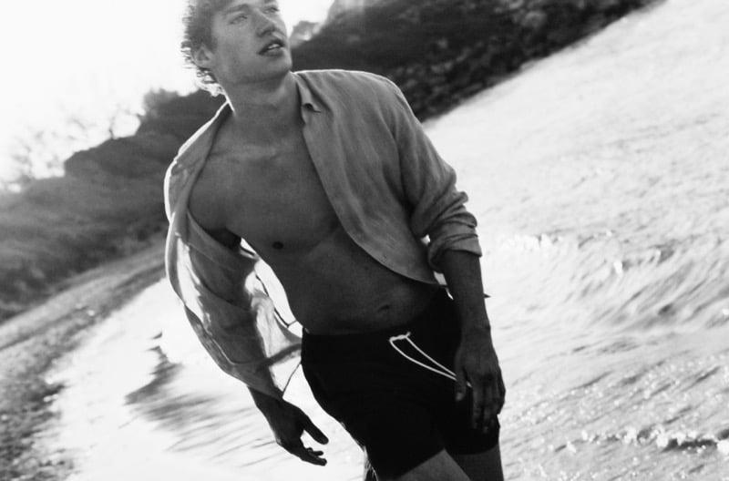 Black and white image of Valentin in an open linen shirt and dark Massimo Dutti swim shorts emerging from the surf