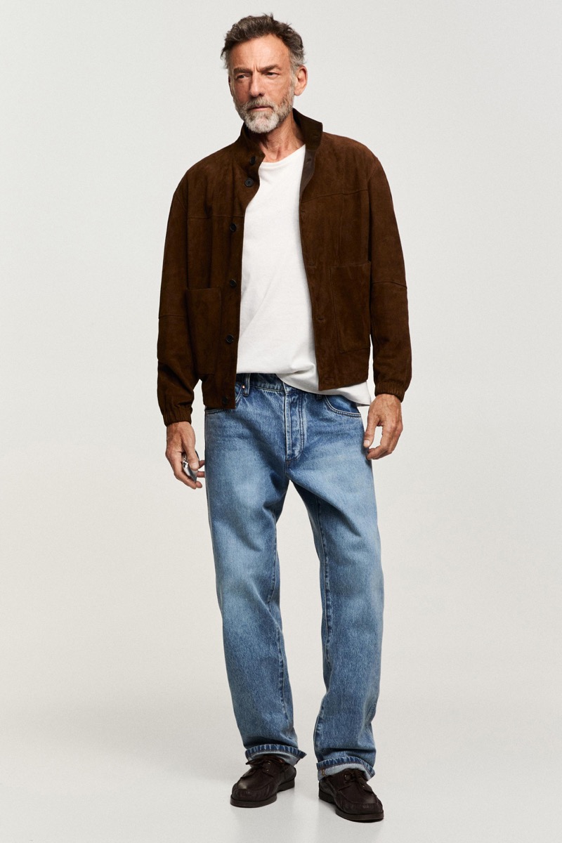 Alain wears a brown suede jacket over a white tee with jeans
