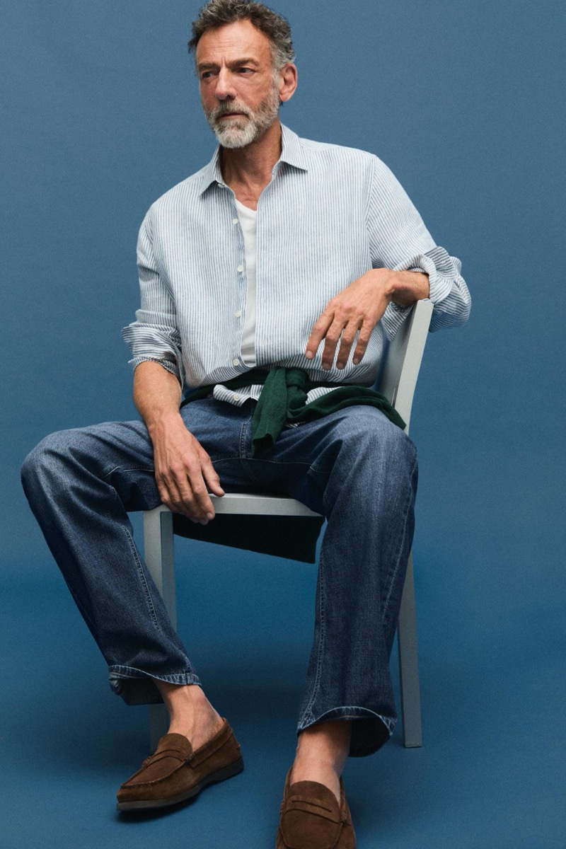 Alain sits in a striped linen shirt with a green sweater tied at the waist