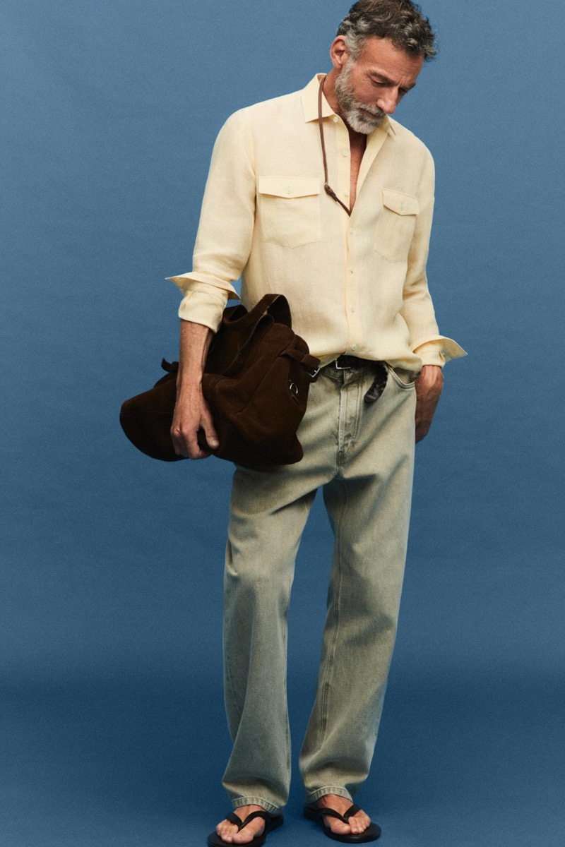 Alain wears a pale yellow linen shirt with jeans and sandals