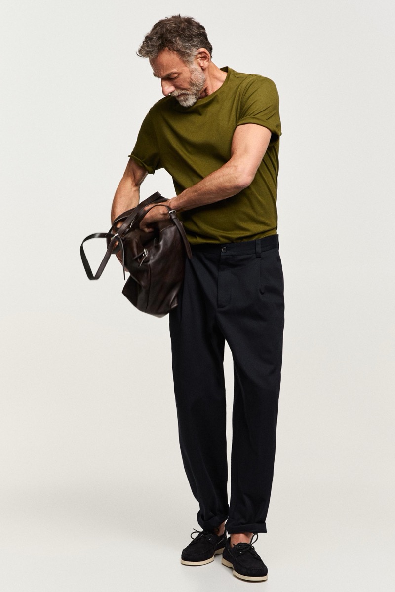 Alain opens a brown leather bag in an olive T-shirt and dark pleated trousers