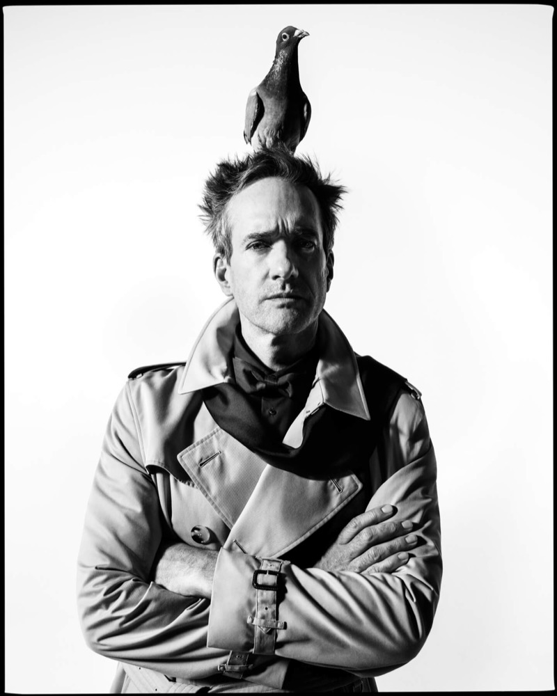 Macfadyen wears a Burberry Kensington trench with a bow tie and a pigeon perched on his head
