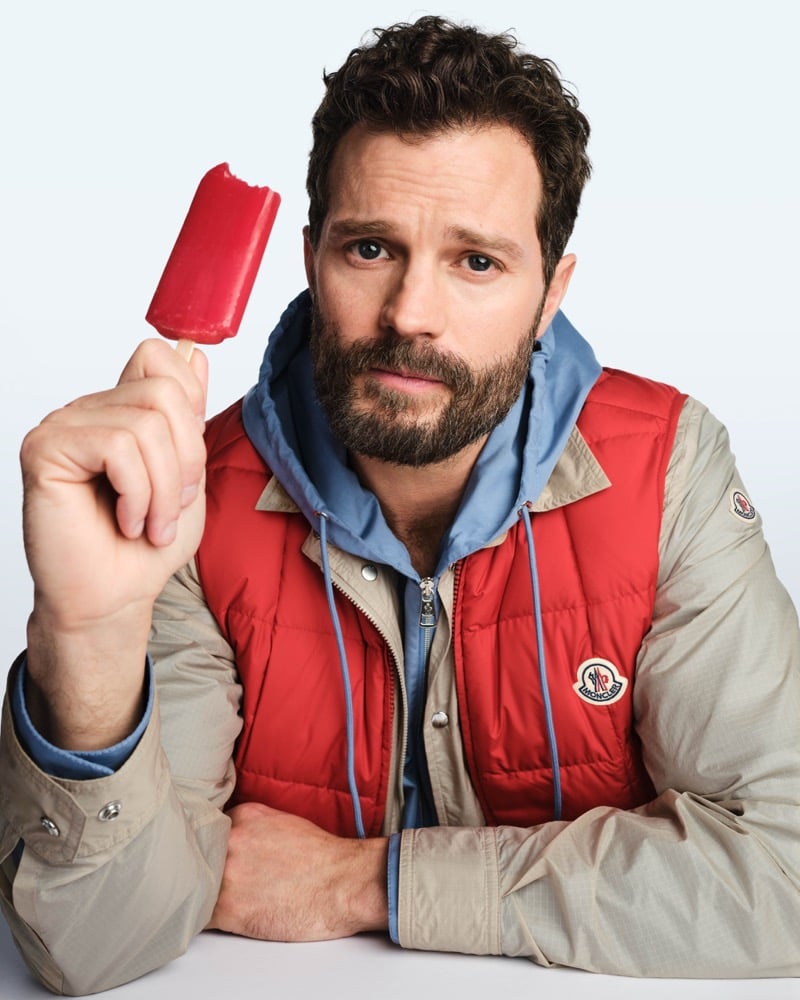 Jamie holds a red popsicle in a red down gilet layered over beige and blue jackets