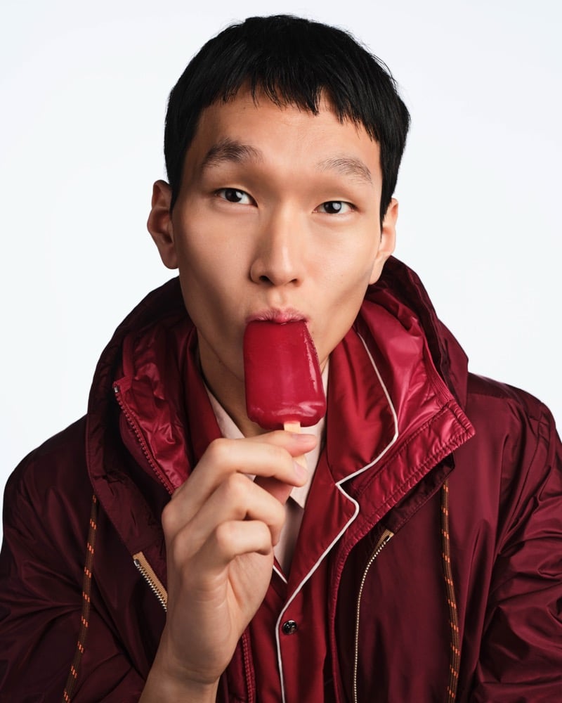 Jun Yeong eats a red popsicle wearing a burgundy Moncler jacket