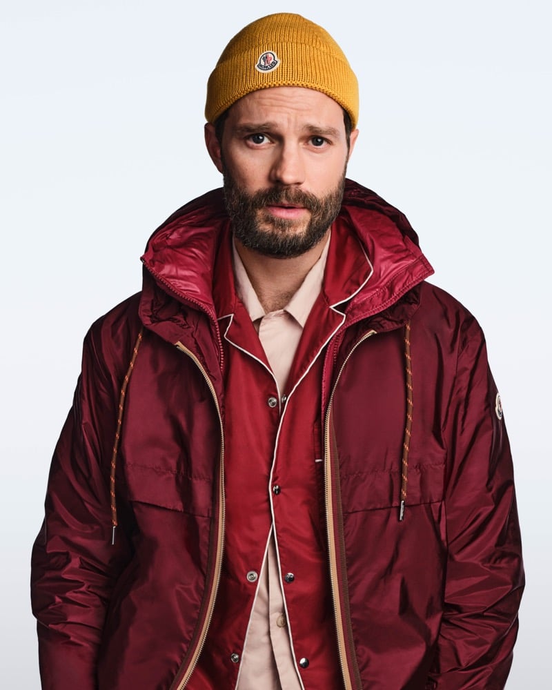 Jamie wears a mustard Moncler beanie with a burgundy windbreaker layered over a red pajama-style shirt